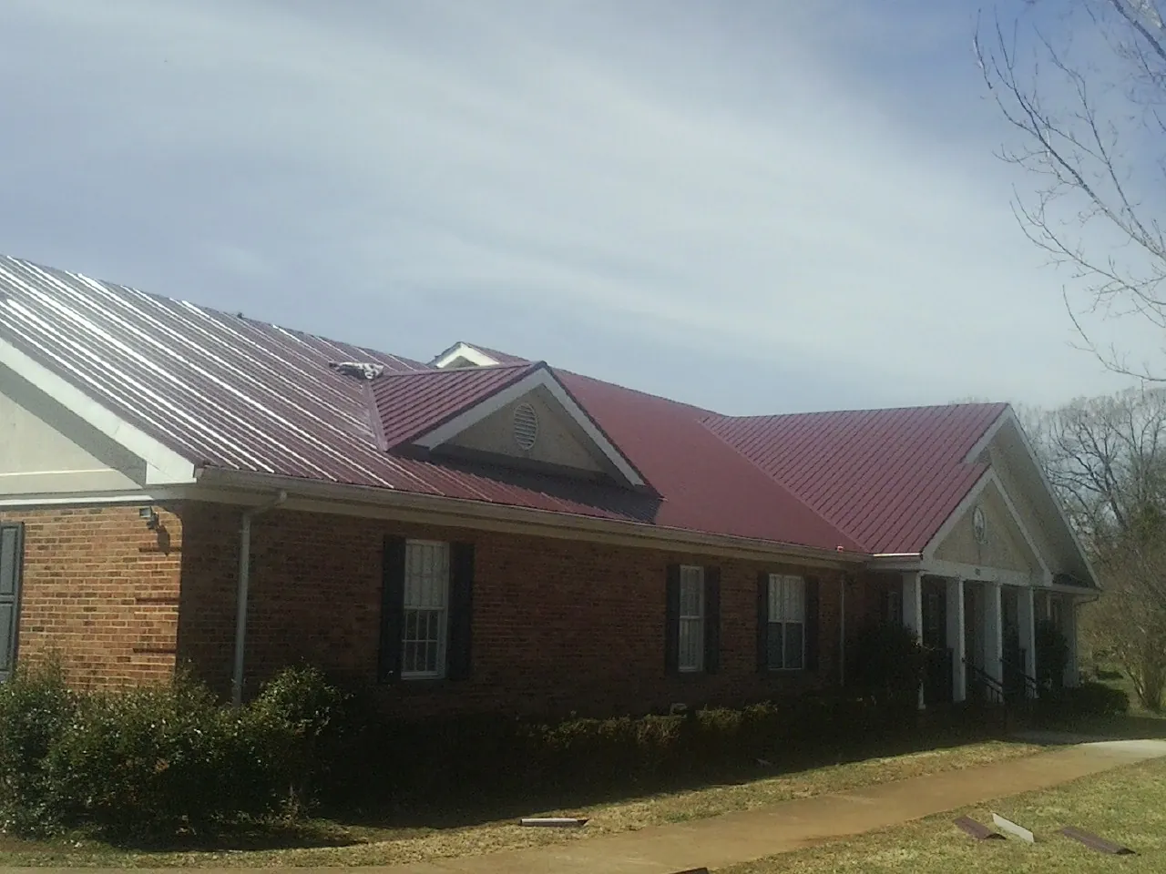 Red metal roof with gabled entries on a long brick building, from a Hail Damage Roof Repair job in Northumberland