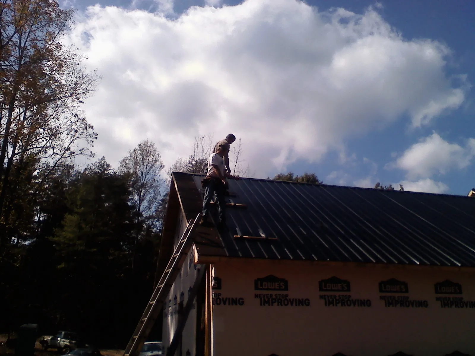 Roofer fastening dark metal panels high against a cloudy sky, from a Roof Inspection job in Northumberland