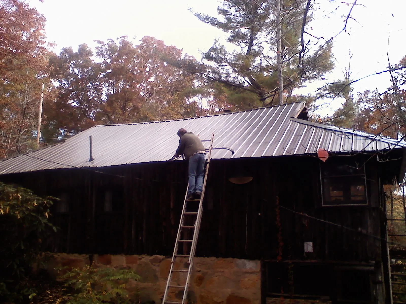 Roofer on a ladder working along the edge of a cabin metal roof in Northumberland