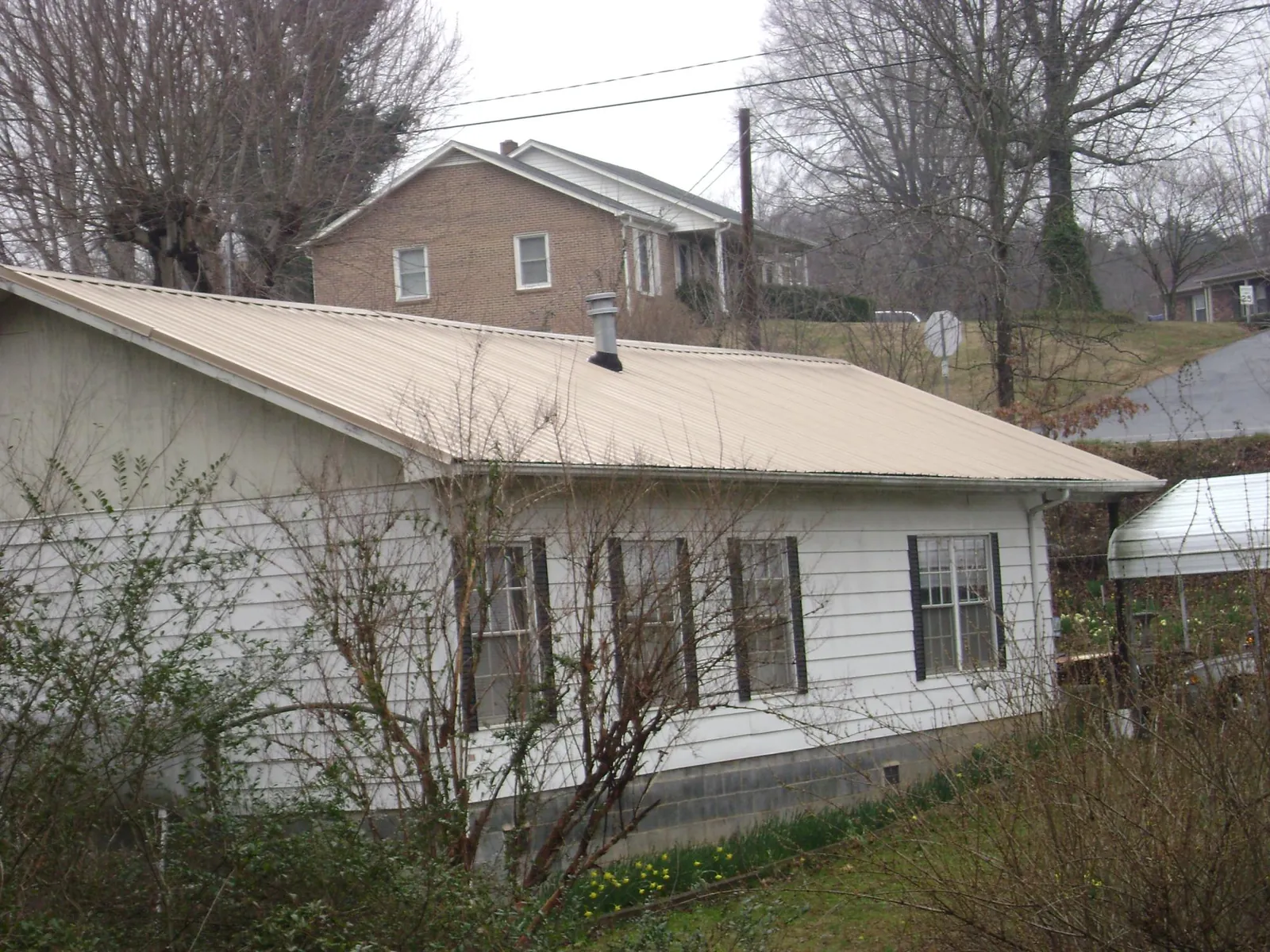 Tan metal roof on a white sided house set into a hillside — Commercial Roofing by Roofing Brothers in Northumberland